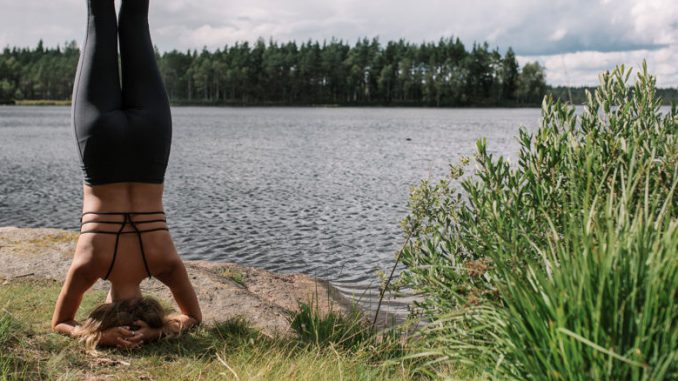 Eine Frau beim Yoga: Kopfstand vor dem schwedischen See.