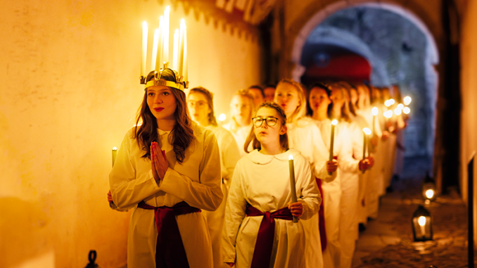 Lucia mit der Krone aus Kerzen schreitet dem Zug voran.